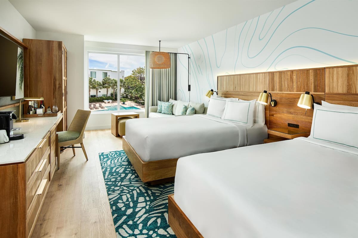 A hotel room with two beds, a desk, a chair, a pool view, and a modern wall design.