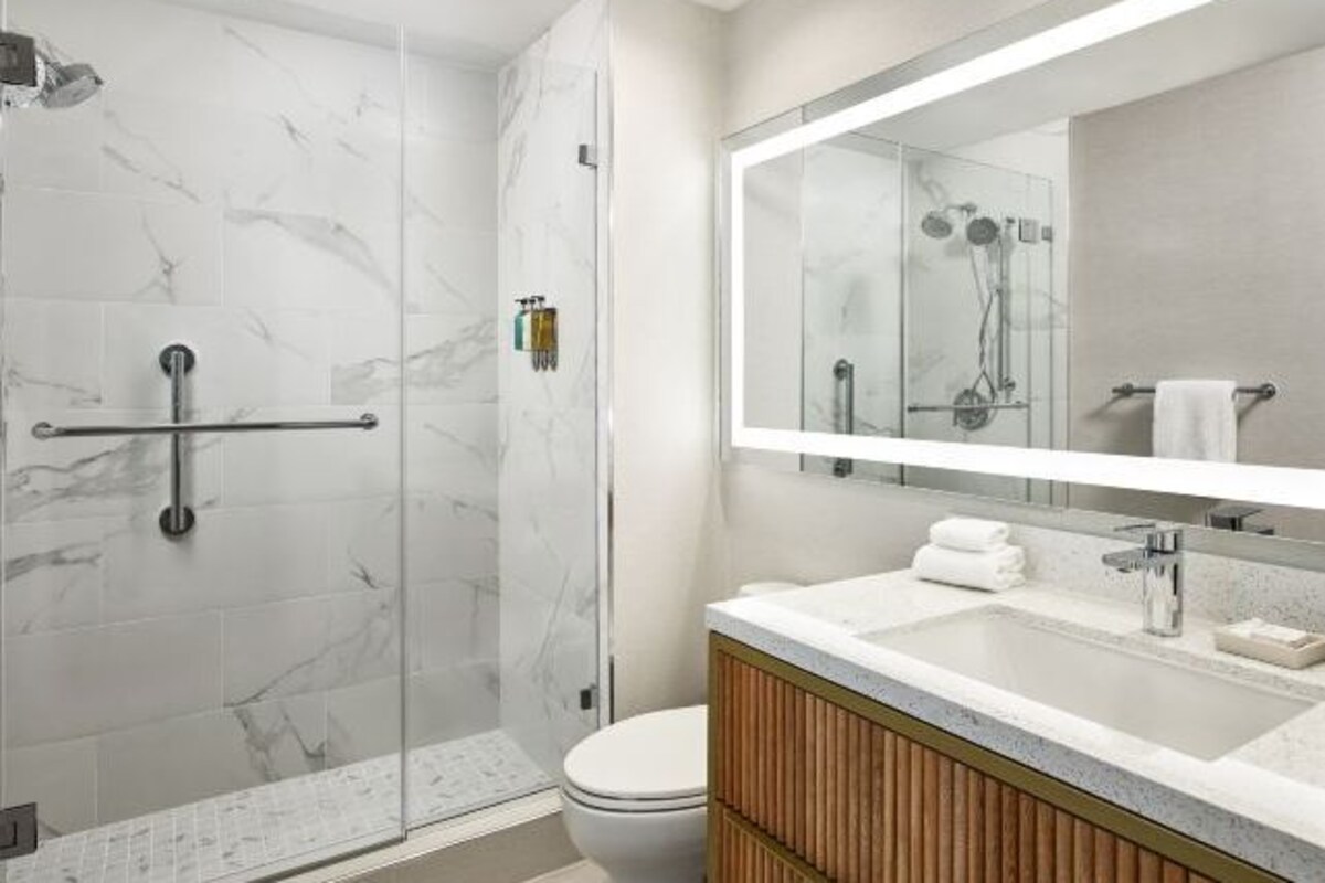 Un baño moderno con cabina de ducha de vidrio, inodoro blanco y tocador con espejo.