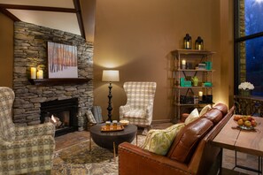 A cozy living room with a stone fireplace, leather sofa, patterned armchair, and a coffee table with drinks.