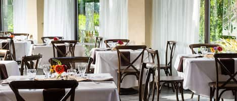 A restaurant with multiple tables set for dining, featuring white tablecloths and wooden chairs.