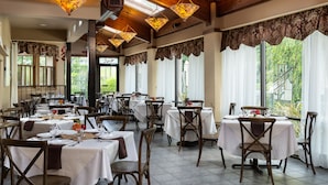 A restaurant with multiple tables and chairs, large windows with curtains, and hanging light fixtures. - Meadowbrook Inn (Blowing Rock)