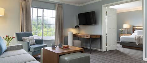 A hotel room with a large window, a flat-screen TV, a desk, a comfortable seating area, and a bed.