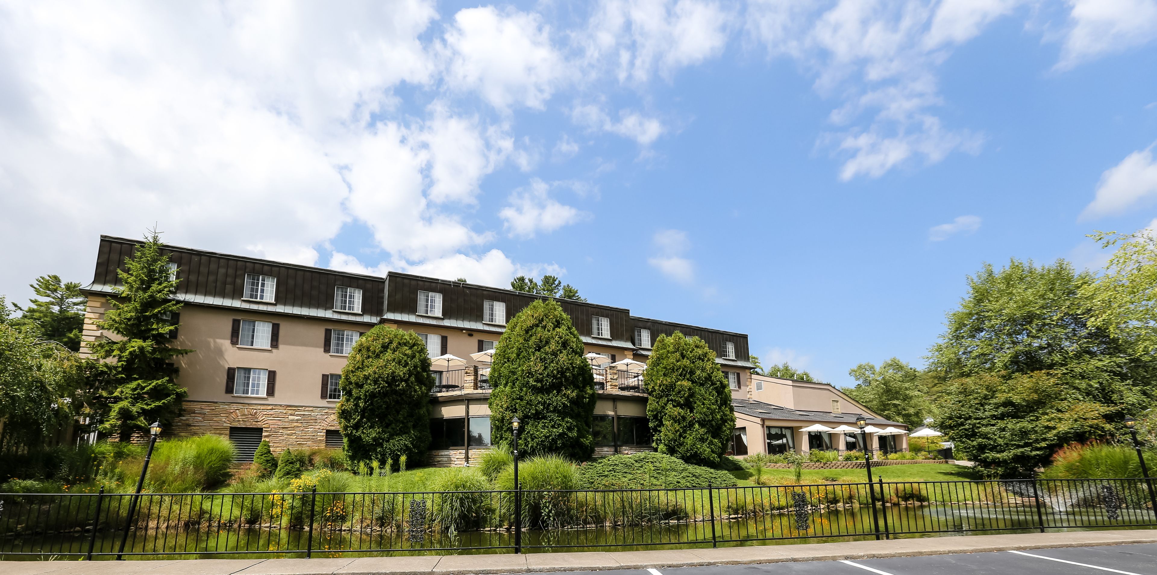 A multi-story hotel with a stone facade, balconies, and a landscaped garden with a pond.