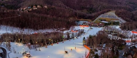 A ski resort with a large snow-covered area, a parking lot, and a road curving around the resort.