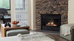 A cozy living room with a stone fireplace, a comfortable seating area, and a table with a bowl of fruit and a remote control.