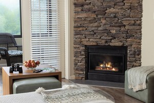 A cozy living room with a stone fireplace, a comfortable seating area, and a table with a bowl of fruit and a remote control.