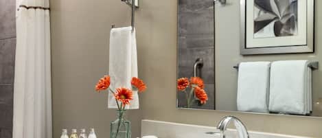 A modern bathroom with a white sink, a glass vase with orange flowers, and a framed picture on the wall.