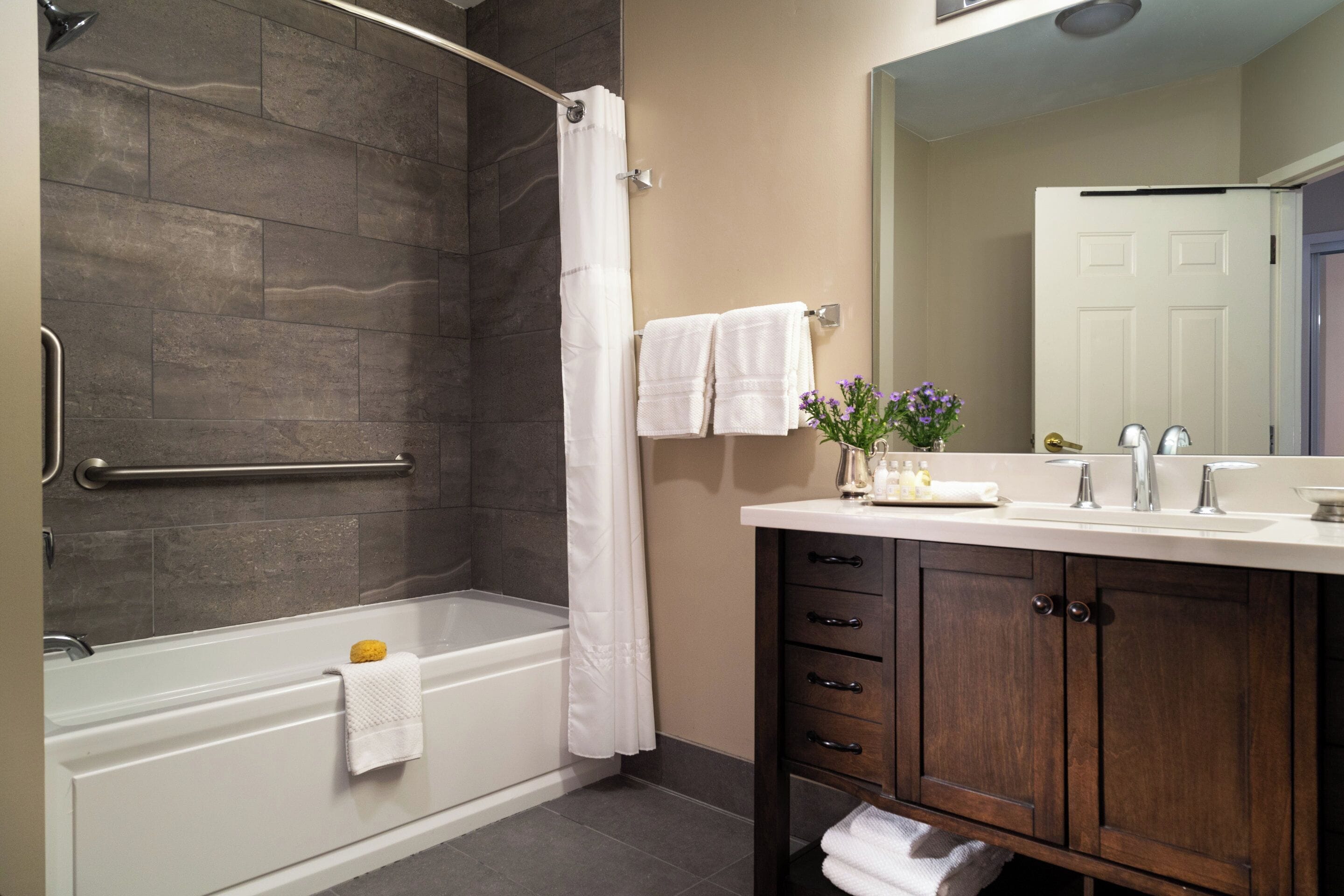 A modern bathroom with a bathtub, shower, vanity, and a large mirror.