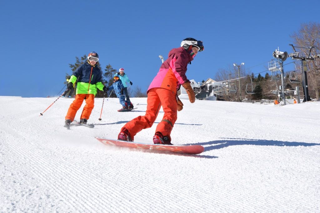 Skiers on a snowy slope with ski lifts in the background.
