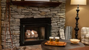 A stone fireplace with a fire, a tray with two glasses of beer, a bowl of popcorn, and a lamp. - Meadowbrook Inn (Blowing Rock)