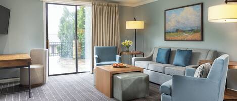 Habitación de hotel con sofá, sillones, una mesa de centro, escritorio y un cuadro en la pared.