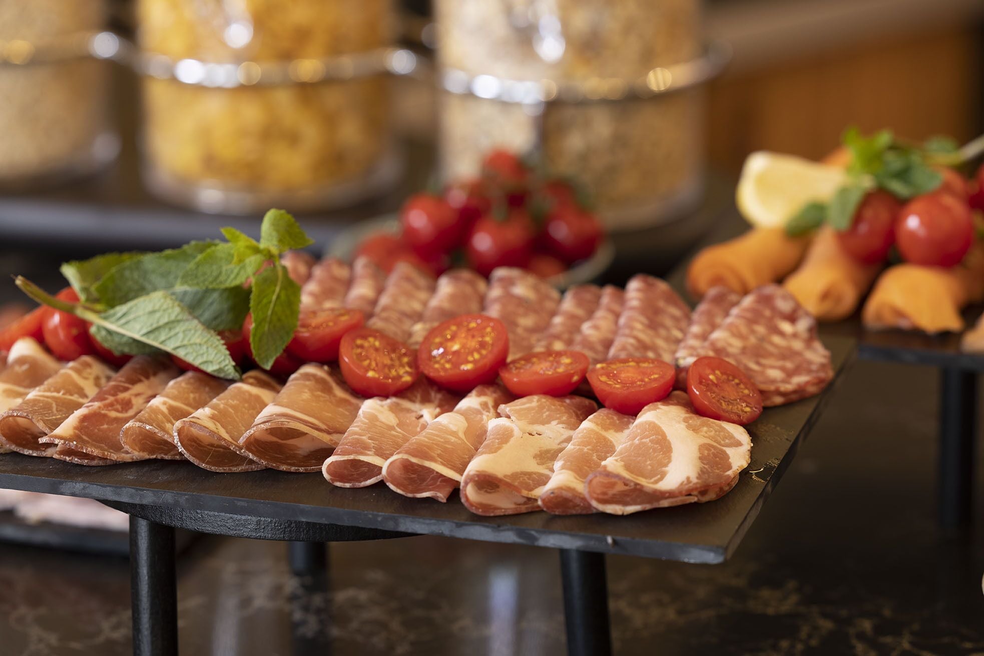 A charcuterie board with various meats, tomatoes, and herbs.