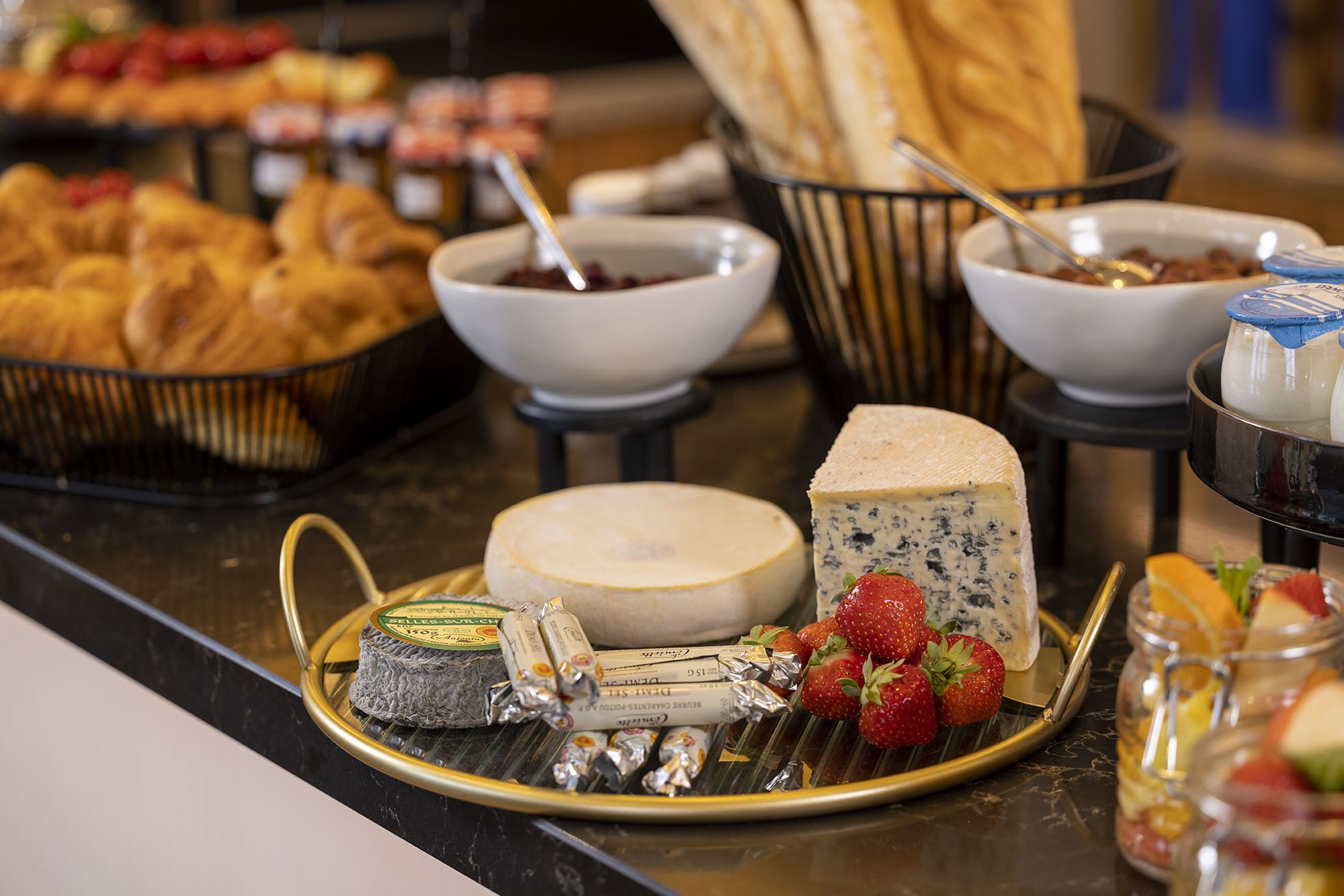A buffet with various cheeses, fruits, and pastries.