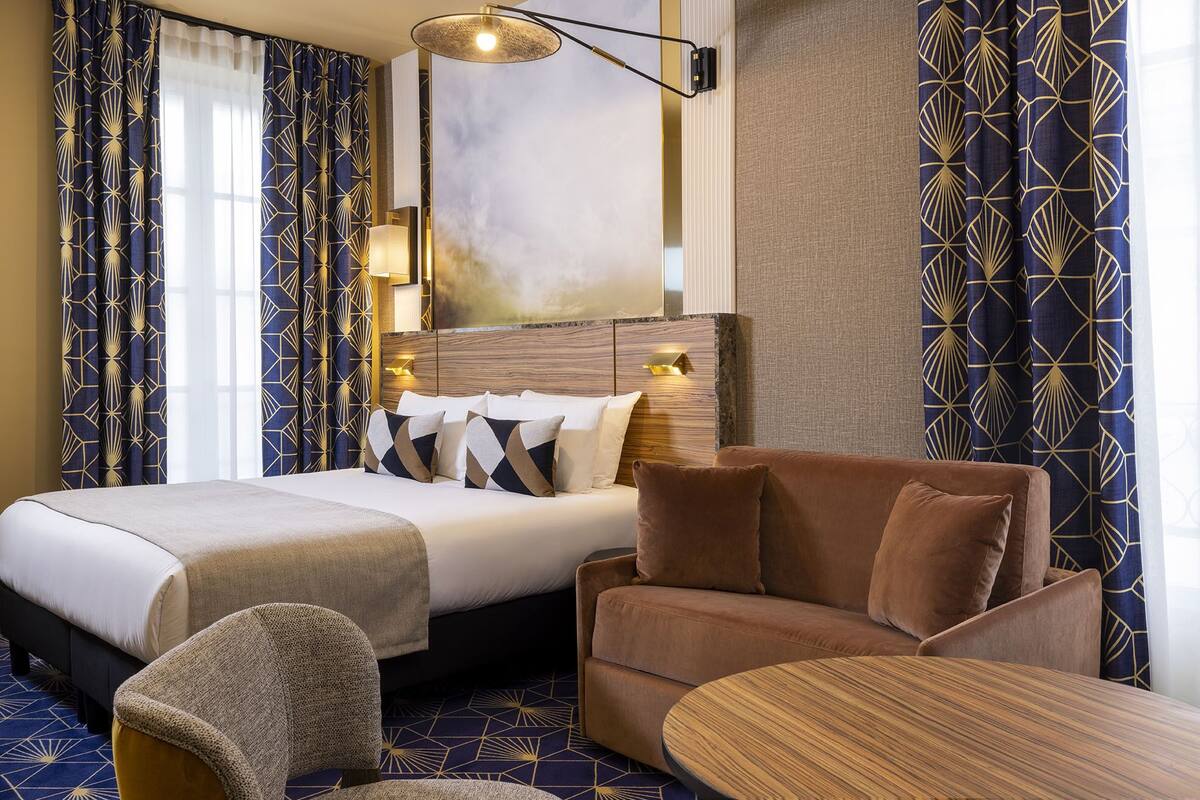 A hotel room with a bed, a sofa, a chair, and a small table.