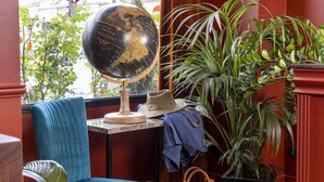 A room with a globe on a stand, a blue chair, a hat, a handbag, and a potted plant. - Hotel Le Rocroy (Paris)