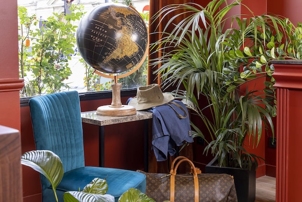 Una habitación con un globo terráqueo sobre un atril, una silla azul, un sombrero, un bolso de mano y una planta en maceta.