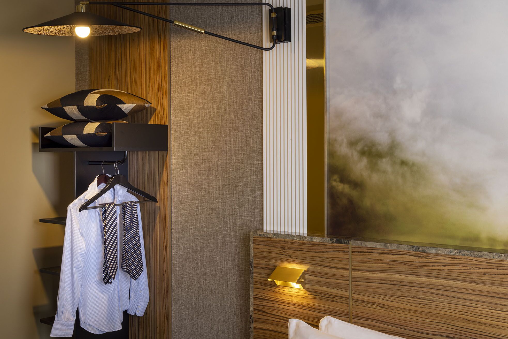 Habitación de hotel con cabecera de madera, lámpara fijada a la pared, pared con textura y un cuadro abstracto grande.