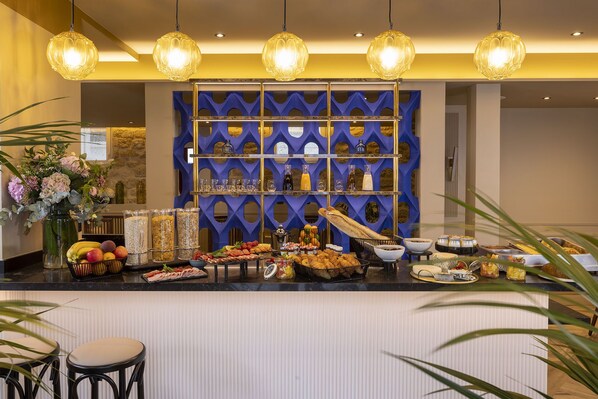 Un área de bufé con diferentes opciones de comida y bebidas, una pared azul decorativa y lámparas colgantes.