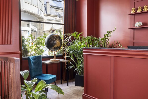 A room with a blue chair, a globe on a table, and various plants. - Hotel Le Rocroy (Paris)
