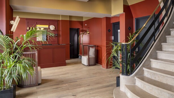 A modern lobby with a wooden floor, a reception desk, a staircase, and potted plants. - Hotel Le Rocroy (Paris)