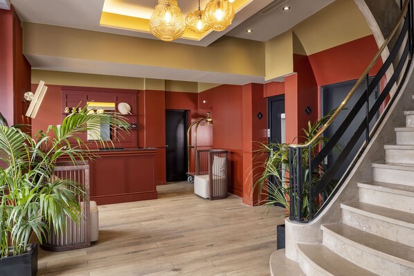 A modern lobby with a wooden floor, a reception desk, a staircase, and potted plants. - Hotel Le Rocroy (Paris)