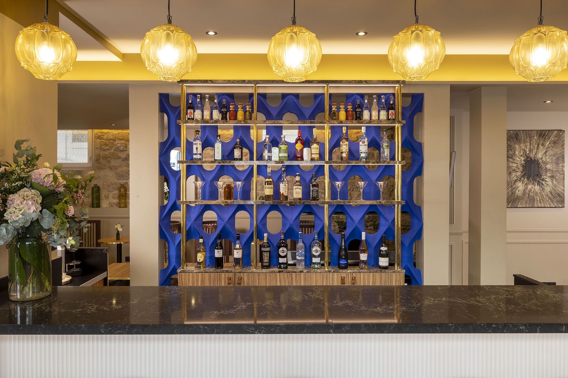 A bar area with a blue patterned shelf holding various bottles and glasses, a marble countertop, and hanging pendant lights.