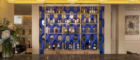 A bar area with a blue patterned shelf holding various bottles and glasses, a marble countertop, and hanging pendant lights.