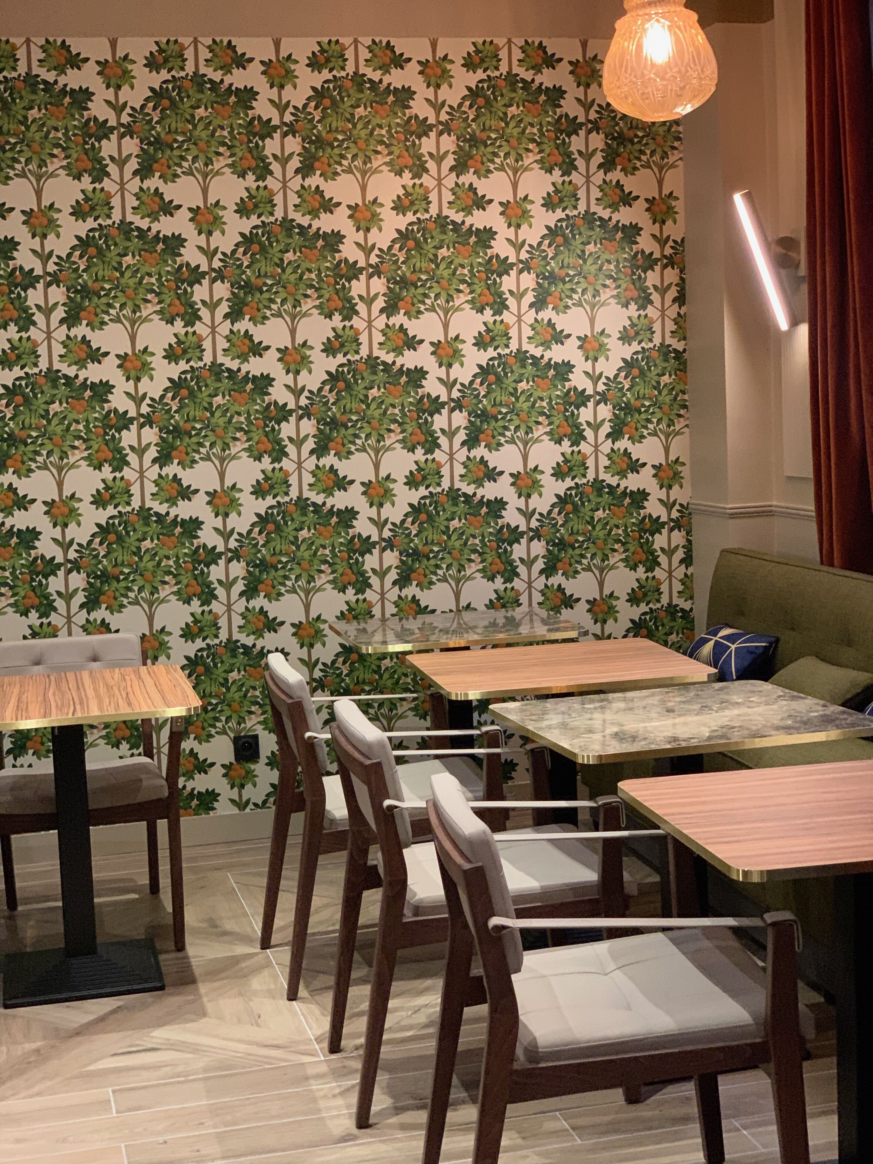 A dining area with wooden tables and chairs, a patterned wallpaper, and a hanging light fixture.