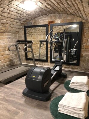 A gym with treadmills, an elliptical, and a stationary bike, with a brick wall and a mirror reflecting the equipment. - Hotel Le Rocroy (Paris)