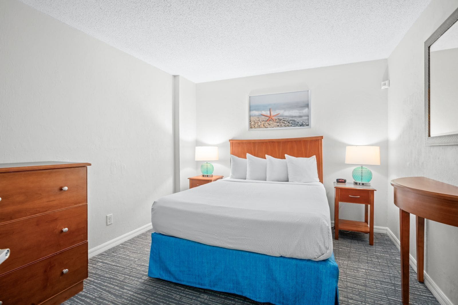 Quarto de hotel com cama, mesas de cabeceira, cômoda e um quadro na parede.