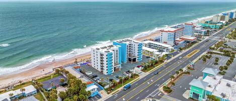 A coastal cityscape with a beach, high-rise buildings, and a road with vehicles.
