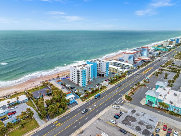 A coastal cityscape with a beach, high-rise buildings, and a road with vehicles. - Tropic Sun Towers (Ormond Beach)