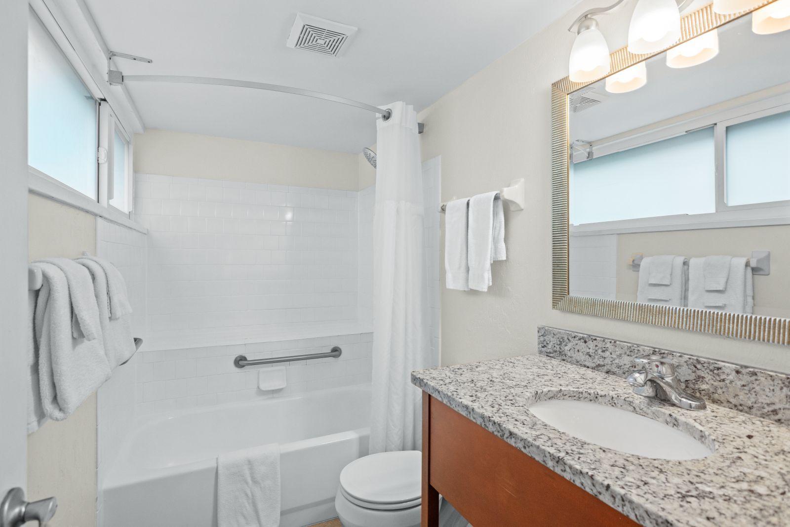 A bathroom with a shower, toilet, sink, and a mirror with lights.