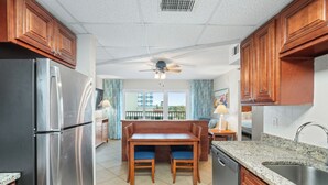 A modern kitchen with wooden cabinets, a stainless steel refrigerator, a granite countertop, and a dining area with a bench and chairs.