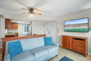 Una sala de estar con un sofá gris, un mueble de entretenimiento de madera y un ventilador de techo.
