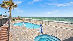 A swimming pool area with two pools, a beach view, and palm trees.