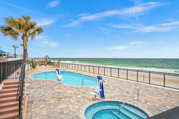 A swimming pool area with two pools, a beach view, and palm trees.