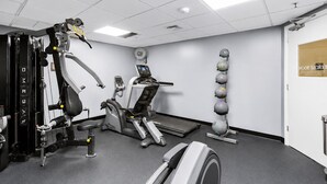 Un gimnasio con máquinas de ejercicio, cinta de correr y un soporte para balones medicinales en la pared.