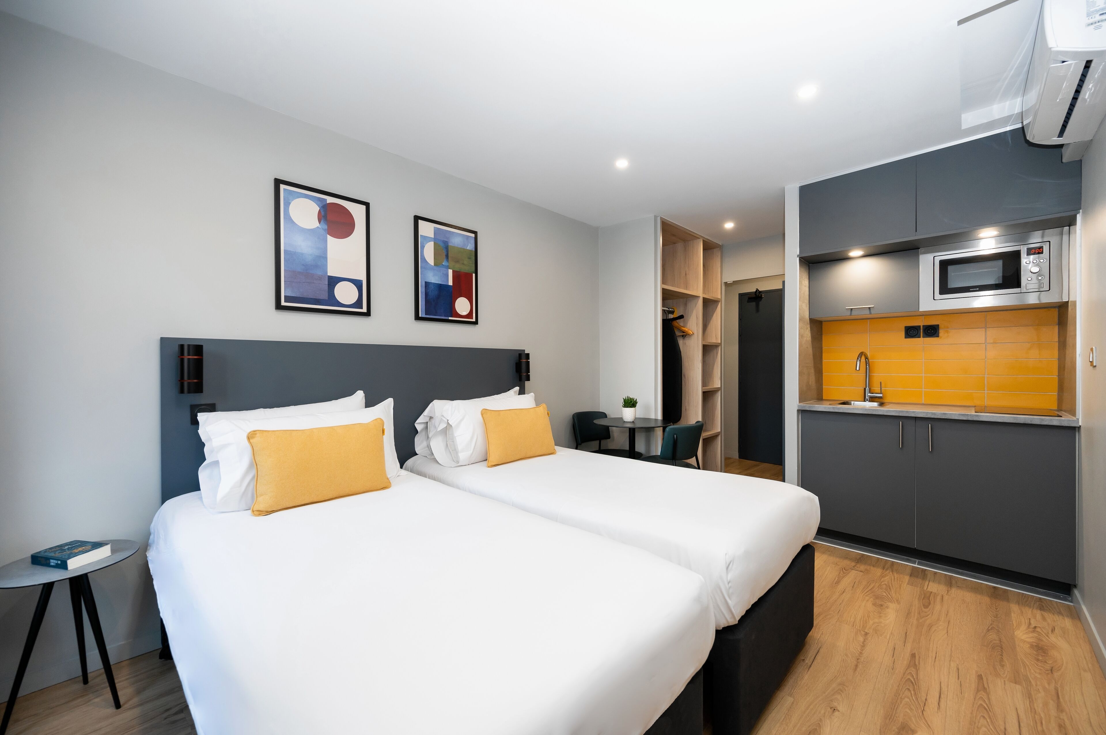 Habitación de hotel con dos camas, una mesita, una silla, microondas y armario.
