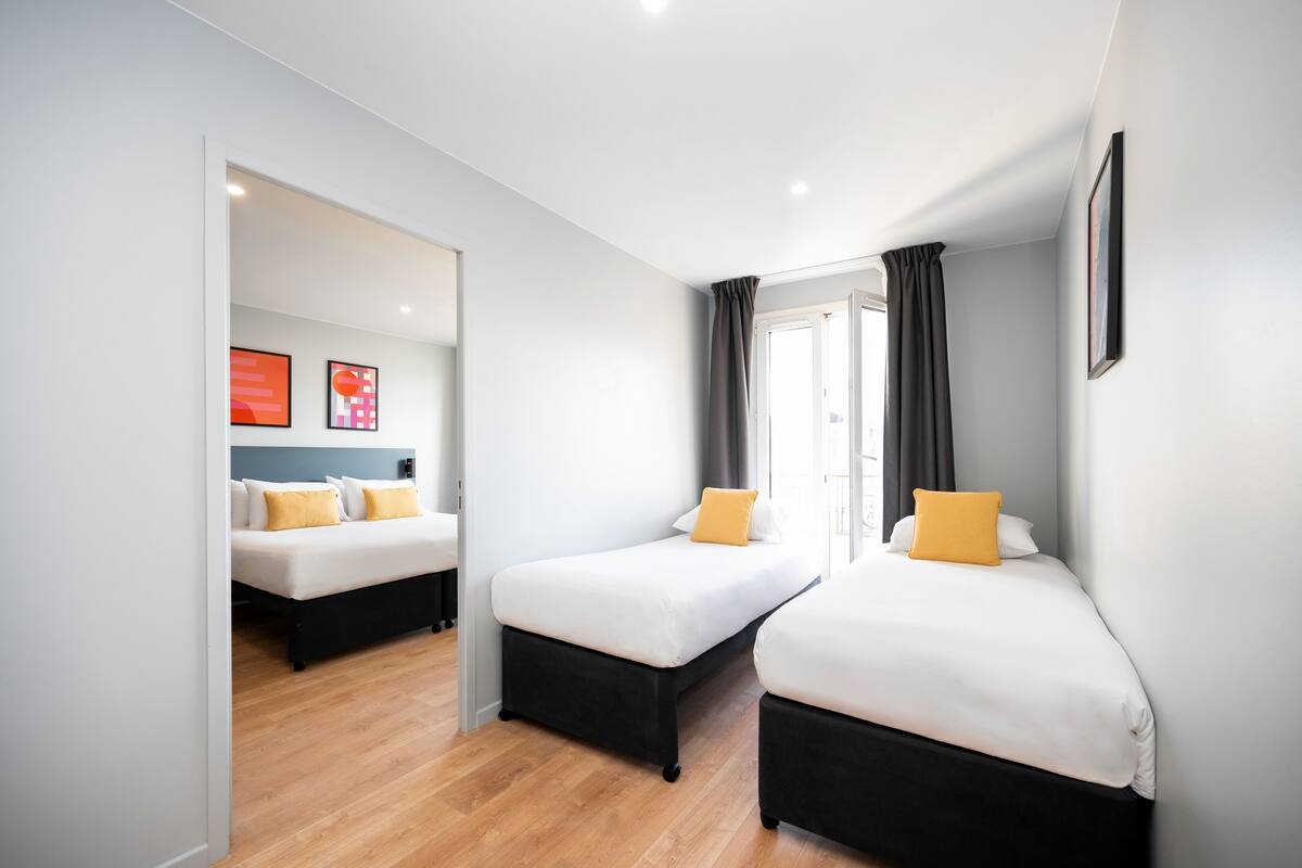 Een moderne hotelkamer met twee eenpersoonsbedden, een houten vloer en uitzicht op de stad.