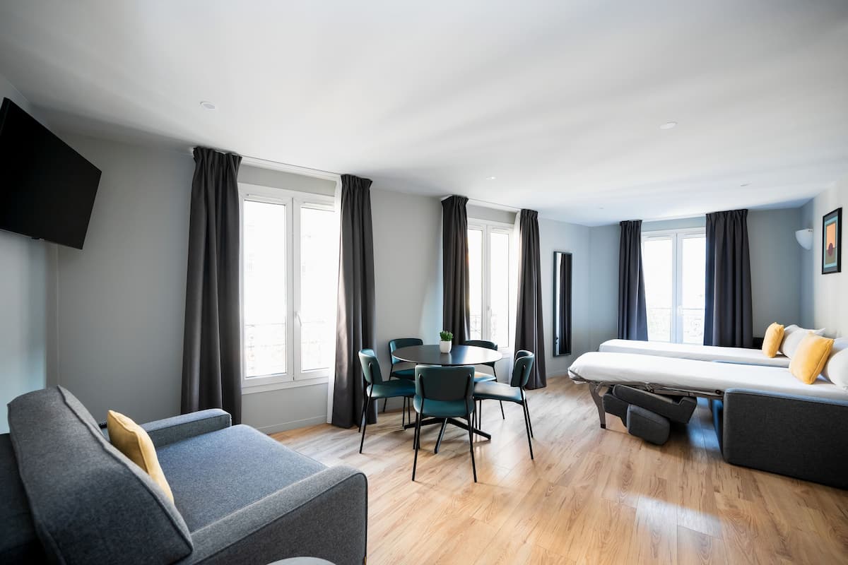 Een moderne kamer met een bank, een eettafel met stoelen, een bed en een wandgemonteerde flatscreen televisie.