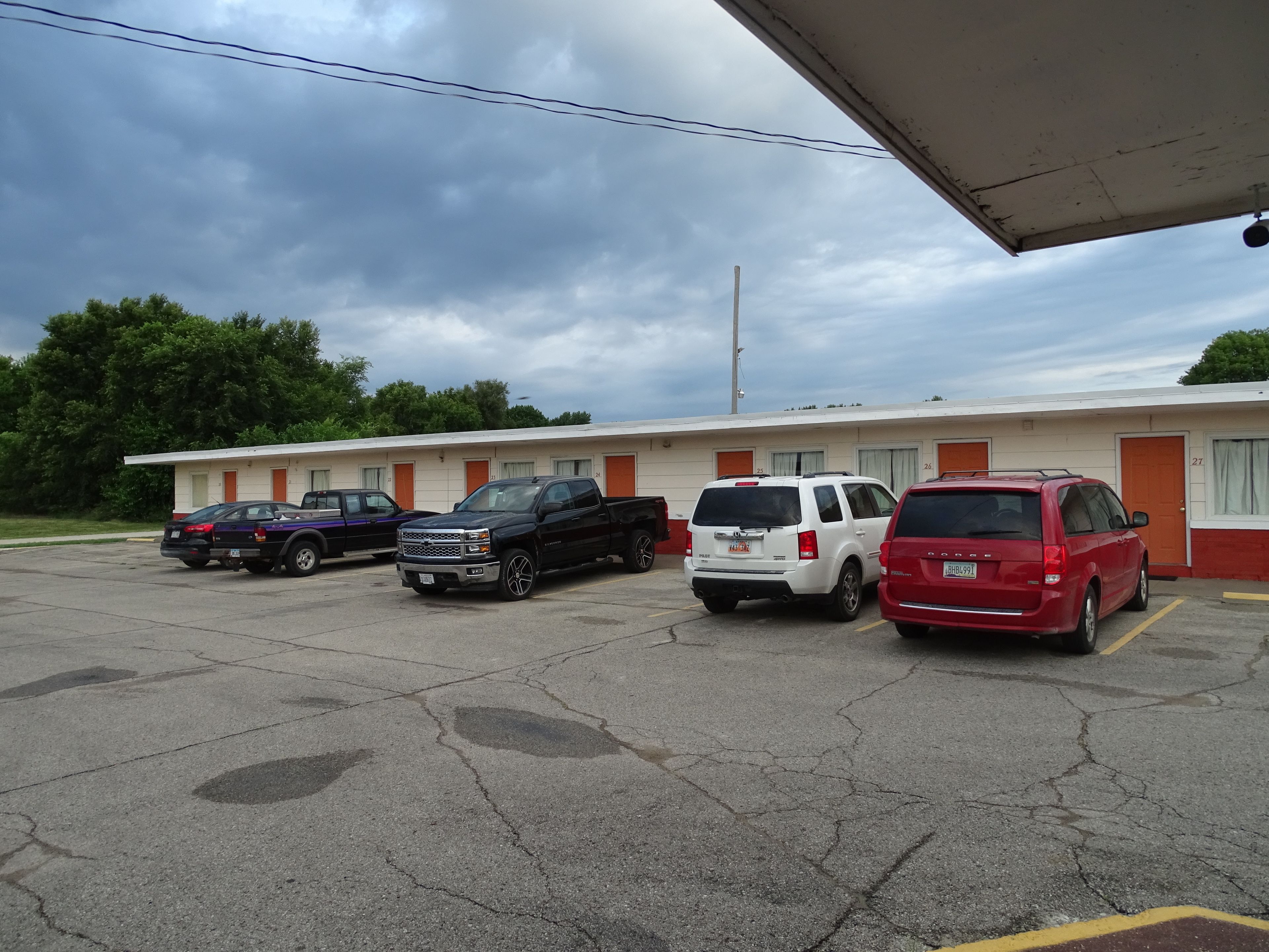 Un motel con una fila de espacios de estacionamiento, un edificio con puertas numeradas y un cielo nublado.