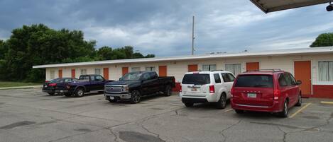 Un motel con una fila de espacios de estacionamiento, un edificio con puertas numeradas y un cielo nublado.