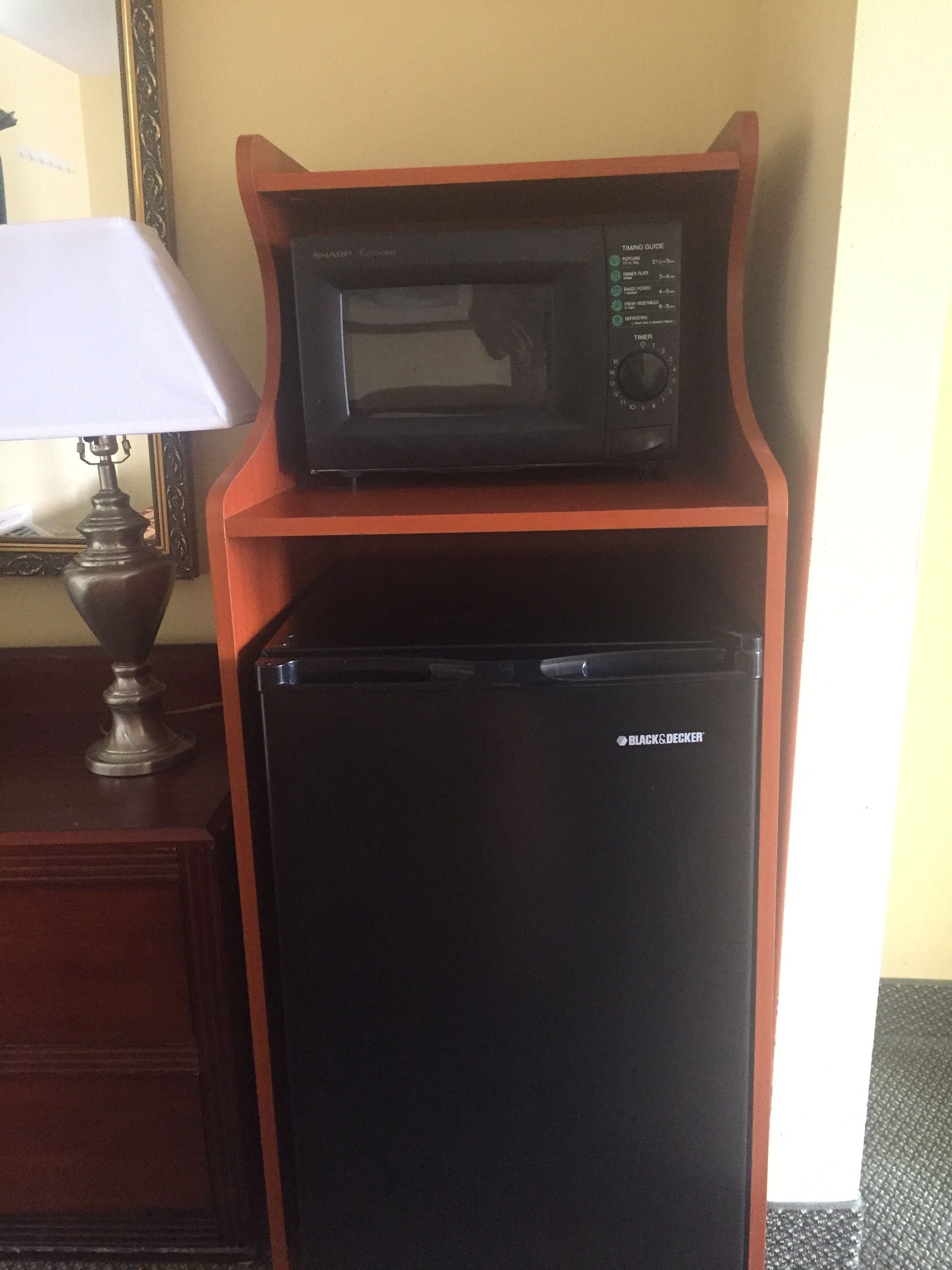 Un refrigerador negro con un microondas encima, sobre un soporte de madera en una habitación.