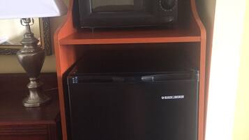 Un refrigerador negro con un microondas encima, sobre un soporte de madera en una habitación.