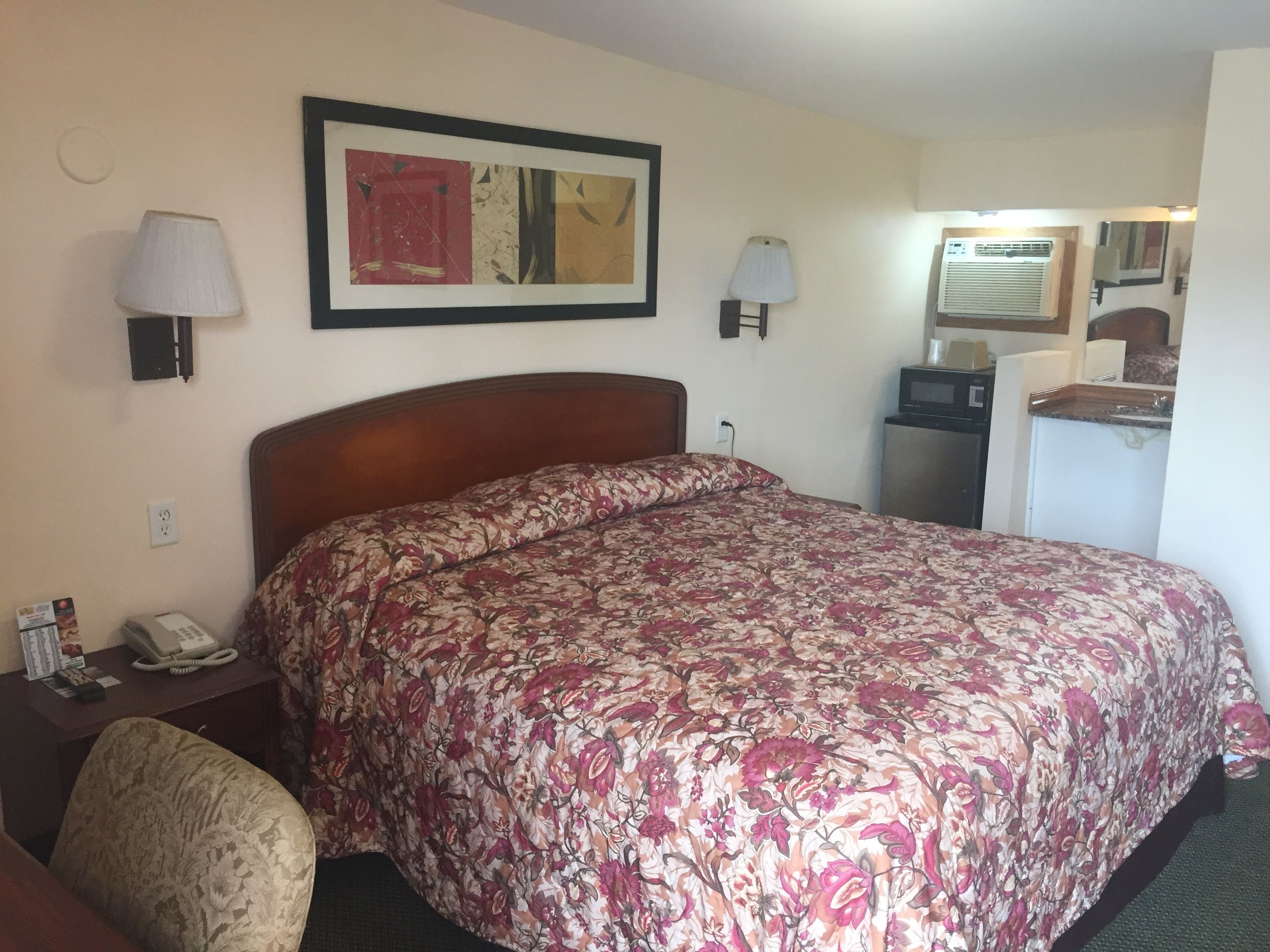 A hotel room with a large bed, a desk with a telephone, a lamp, and a painting on the wall.