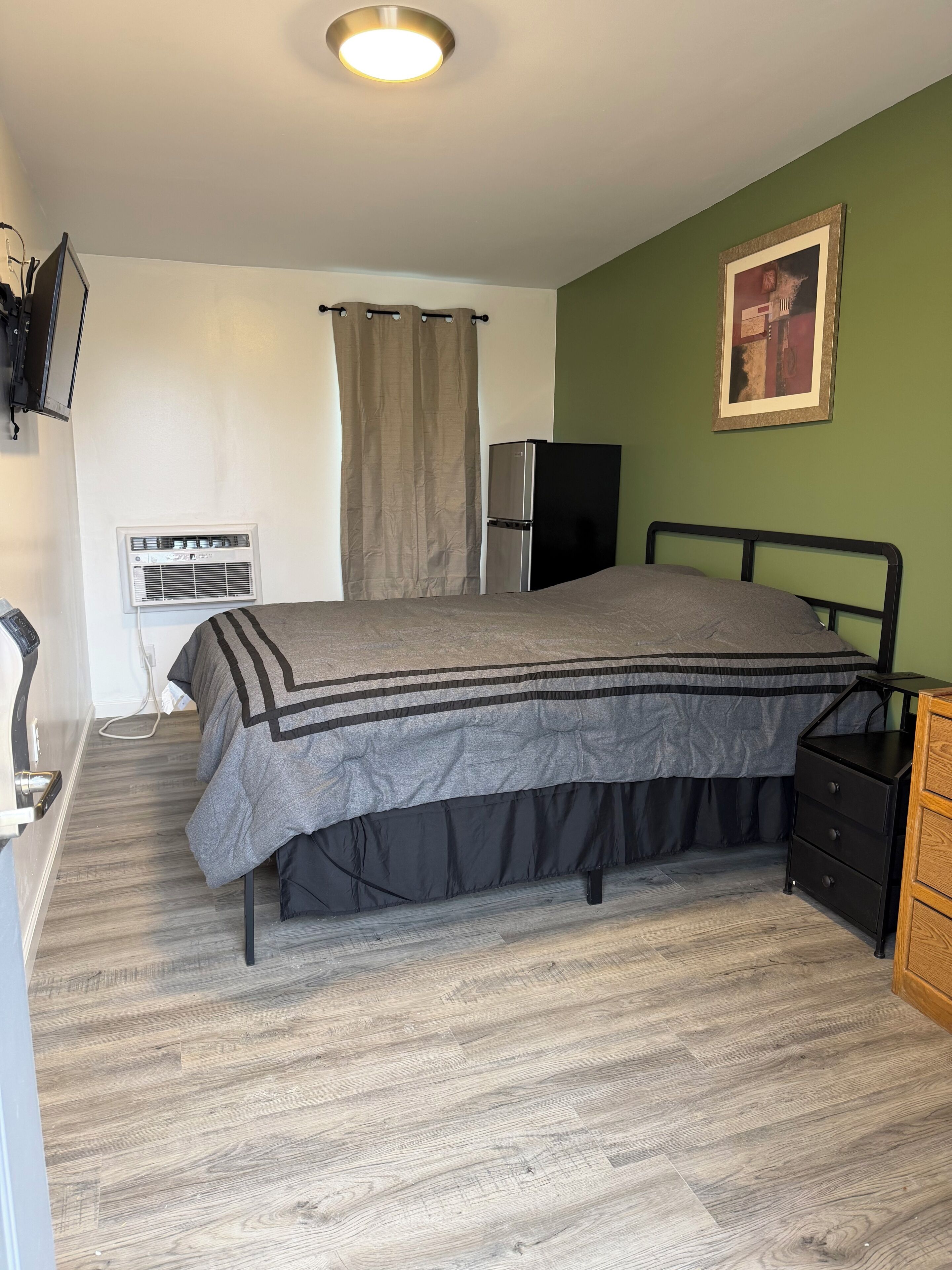 Ein Schlafzimmer mit Bett, Schminktisch, Fernseher, Klimaanlage und einem Bild an der Wand.