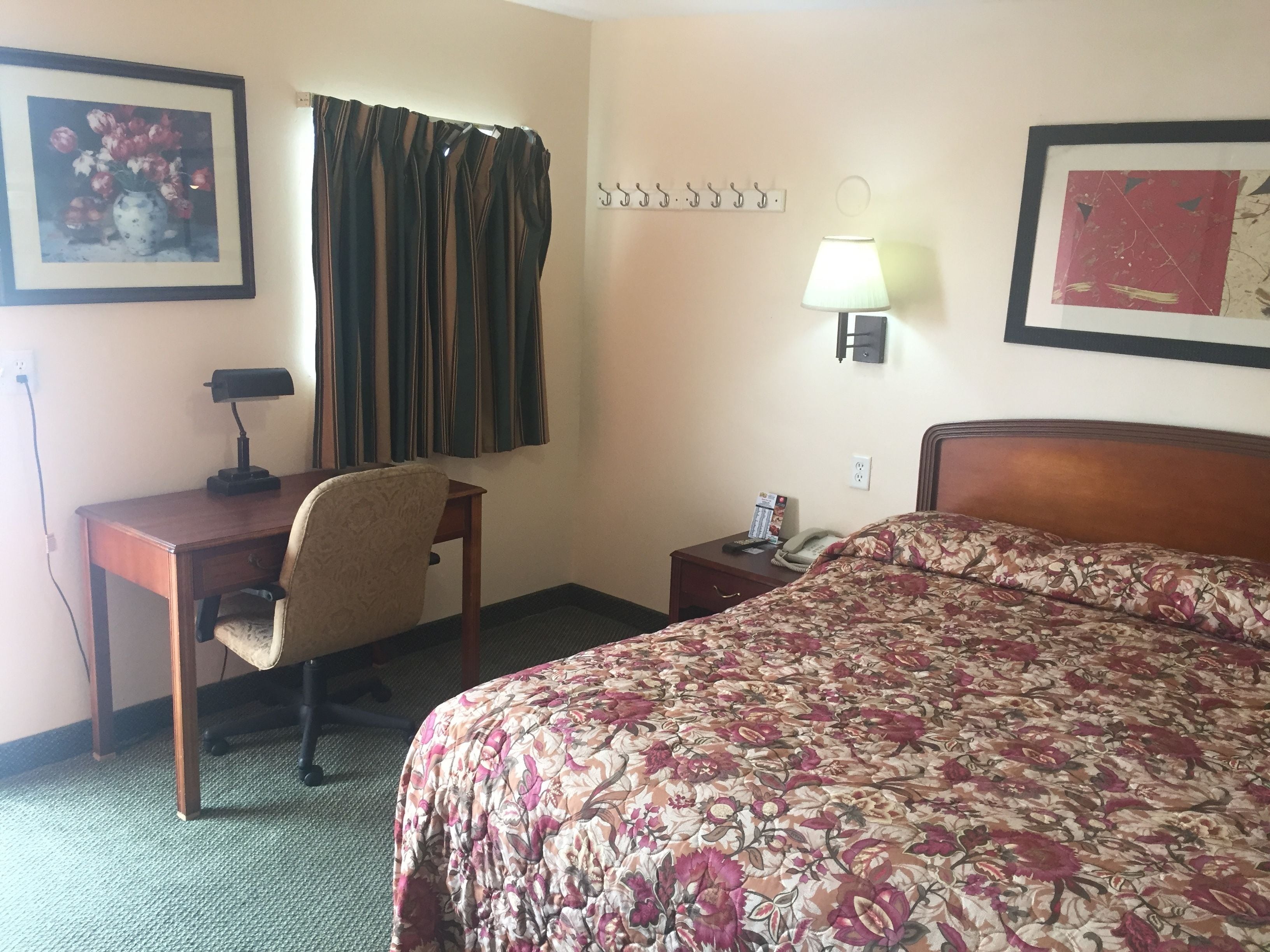 Habitación de hotel con cama, escritorio con silla, lámpara y un cuadro en la pared.