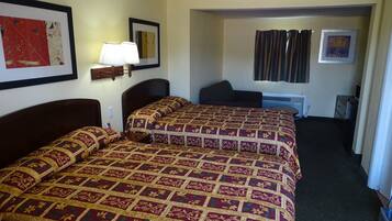 A hotel room with two beds, a desk, a chair, a lamp, and a framed picture on the wall.