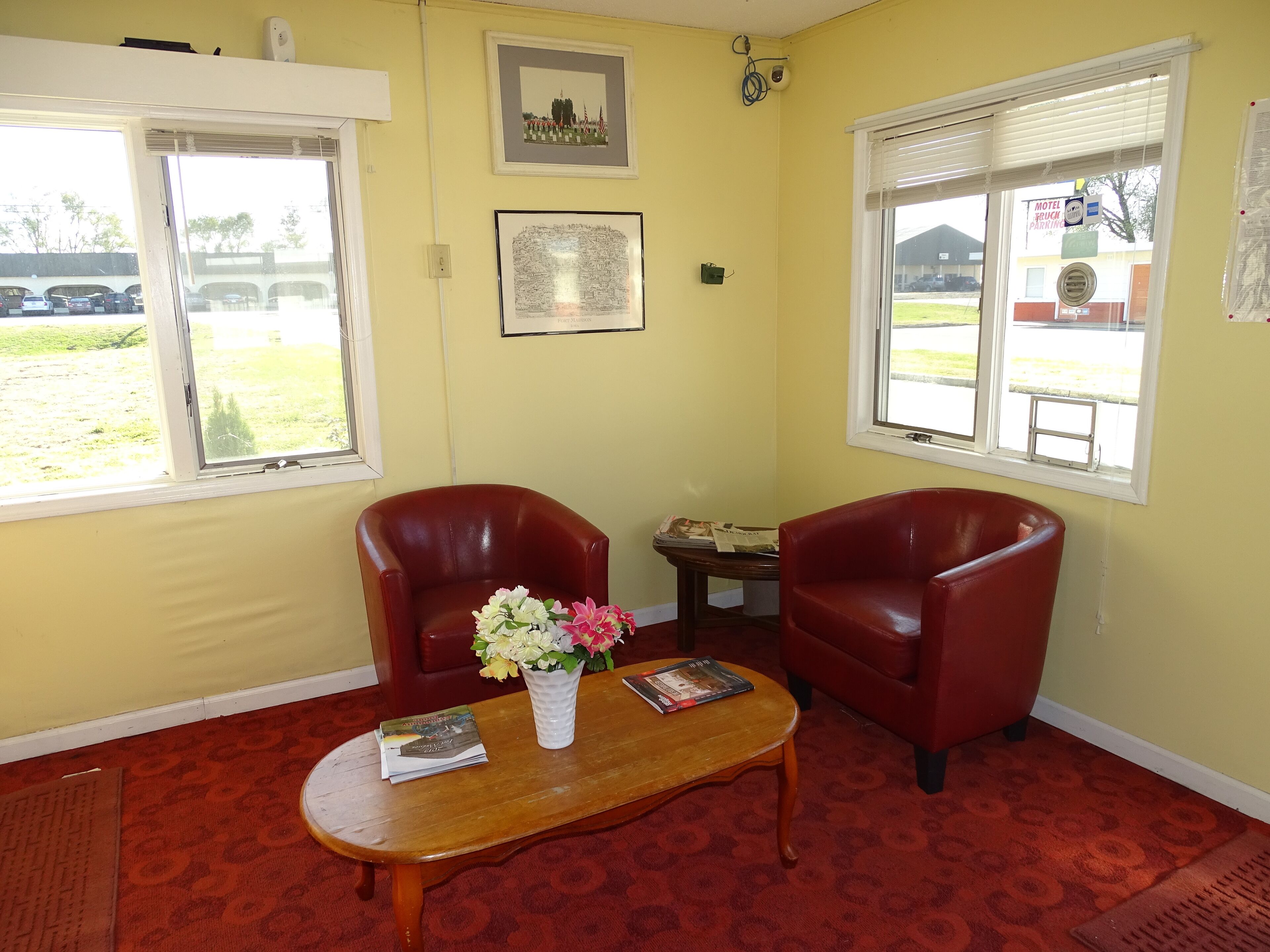 A room with two red leather chairs, a wooden table with a vase of flowers, and a framed picture on the wall.